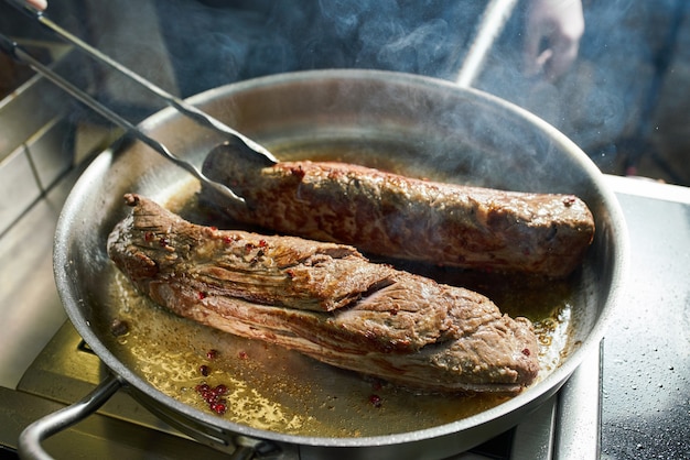 O chef trabalha na cozinha do restaurante. Carne fresca assada em uma frigideira grande. Fundo de cozinha de restaurante