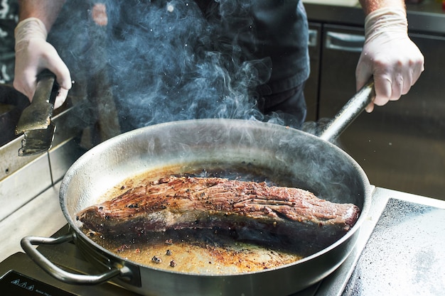 O chef trabalha na cozinha do restaurante. Carne fresca assada em uma frigideira grande. Fundo de cozinha de restaurante