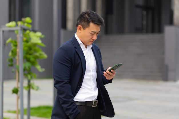 O chefe do empresário asiático olha para o celular, lê notícias do telefone e escreve no messenger fora do escritório