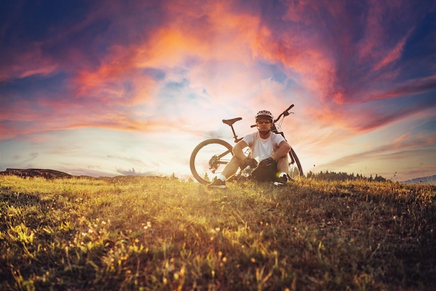 O ciclista está sentado em um prado enquanto descansa de um passeio extenuante em estradas de montanha O ciclista é resfriado pela água Foco seletivo Foto de alta qualidade