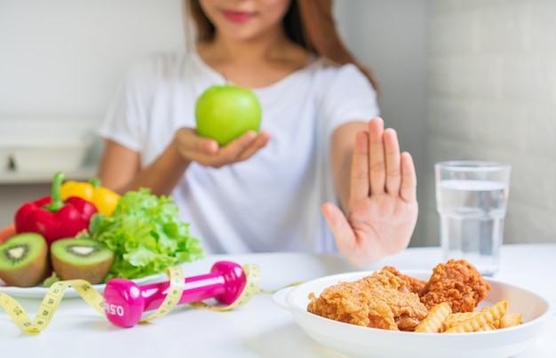 O close-up da jovem mulher asiática que usa a mão retira seu frango frito favorito, batatas fritas e escolhe a maçã verde, frutas e legumes para a boa saúde. mulher no conceito de dieta. fechar-se