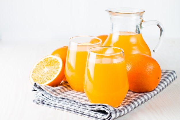 O close-up de um vidro do suco de laranja com laranjas frutifica no fundo de madeira.