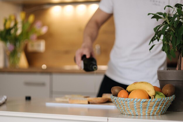 O close up do homem espalha o azeite na baguete Interior brilhante da cozinha Concentre-se na cesta de frutas