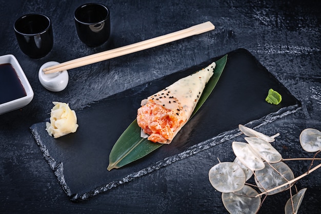 O close-up do sushi saboroso da mão rola no mamenori com salmão e o caviar de tobico servido na placa de pedra escura com molho de soja e gengibre. copie o espaço. temaki, cozinha japonesa. comida saudável