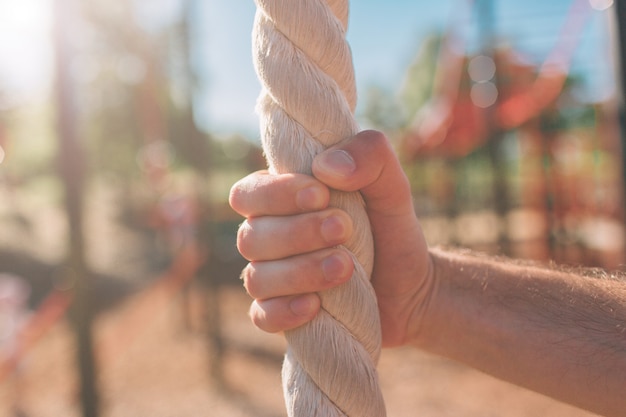 Foto o close up dos braços peludos do homem que agarram ou que guardam uma corda que indica alguém que escala em um gym borrou o fundo. homem musculoso atraente com cordas pesadas nos ombros. foto do homem no sportswear