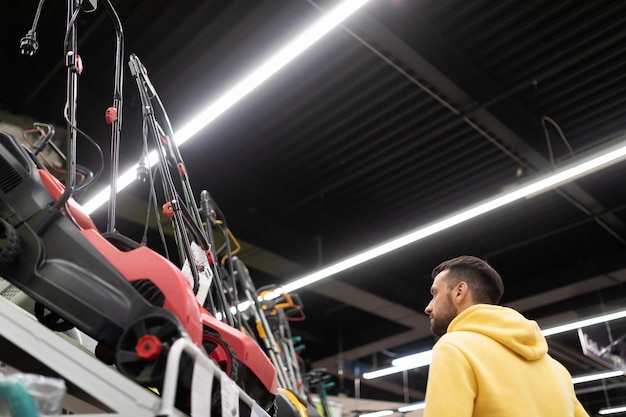 O comprador fica ao lado de um rack com cortadores de grama a gasolina e elétricos