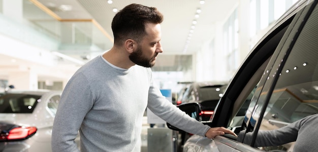 O comprador masculino escolhe um carro novo em uma concessionária de carros inspeciona o carro