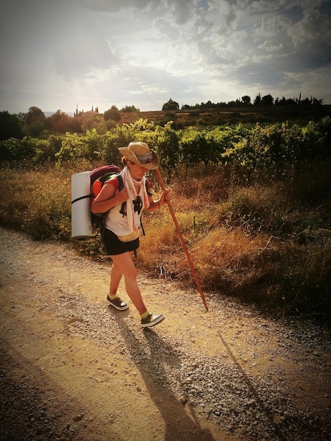 O comprimento total de uma mulher a caminhar por uma estrada de terra contra o céu