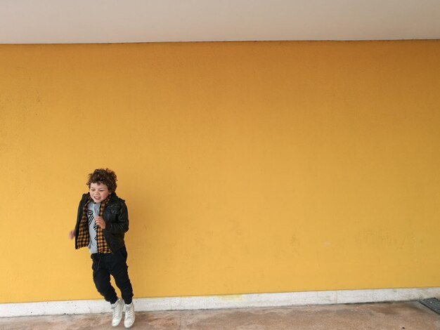 Foto o comprimento total do rapaz a saltar contra a parede amarela