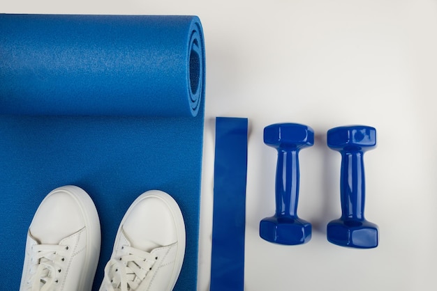 O conceito de acessórios esportivos Foto de tênis brancos barras azuis e um tapete de exercício azul e outros equipamentos esportivos