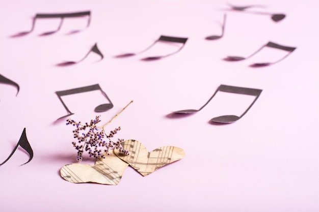 O conceito de amor pela música Dois corações de papel secam flores e notas em um fundo rosa