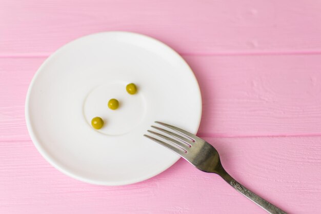 O conceito de bulimia de fome Algumas ervilhas em um prato branco e um garfo