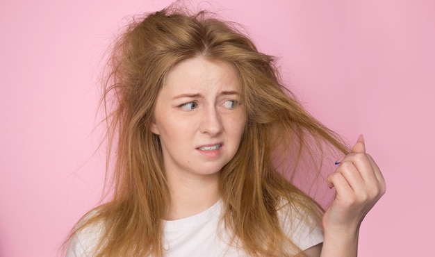 Foto o conceito de cabelo seco e sem vida uma mulher em um fundo rosa mantém-na desordenada