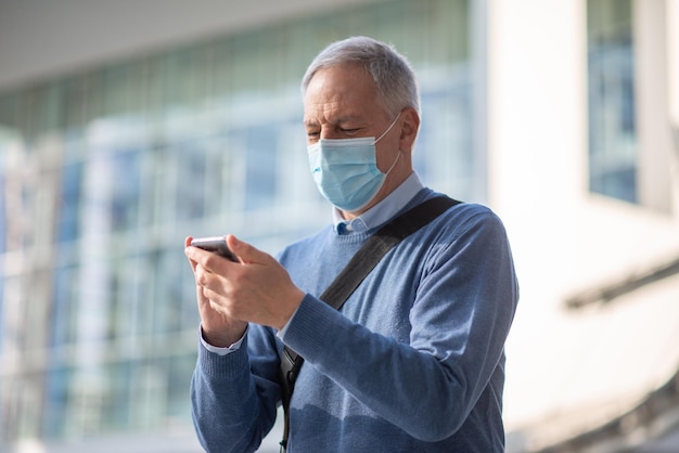 O conceito de coronavírus covid mascarou um homem mais velho usando seu smartphone ao ar livre