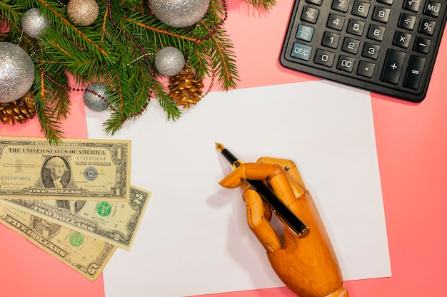 O conceito de dinheiro e Natal. Uma mão de madeira escreve uma carta de Natal para o Papai Noel em papel branco.