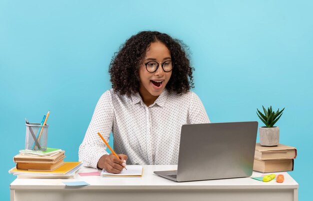 O conceito de educação on-line empolgou uma jovem estudante negra sentada à mesa usando a escrita do laptop