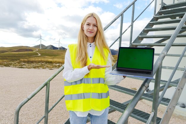 O conceito de energia verde Retrato de uma jovem com um laptop com uma tela verde no fundo das turbinas eólicas