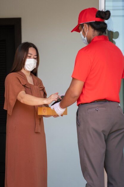 O conceito de entrega segura Um correio em um uniforme vermelho com máscara de proteção para entrega ao cliente