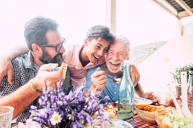 O conceito de família de pessoas felizes ria e se diverte junto com três gerações de idades diferentes: avô, pai e filho adolescente, todos juntos comendo no almoço