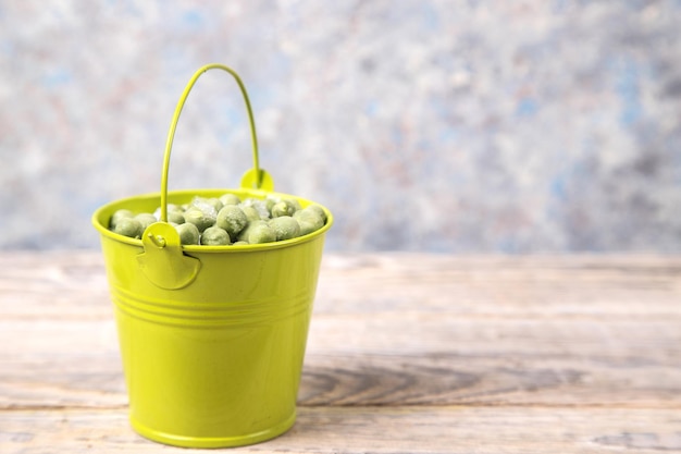 O conceito de legumes congelados ervilhas verdes congeladas em um balde verde sobre uma mesa de madeira leve