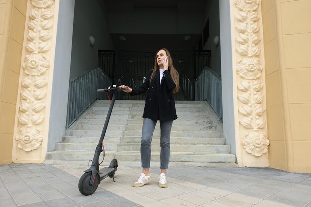 O conceito de transporte ecológico Uma jovem está falando ao telefone perto de uma scooter elétrica