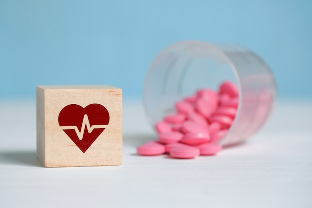 O conceito de uma dose diária de medicação para o coração. Ícone em um quadrado de madeira ao lado de comprimidos feitos de copo de plástico.