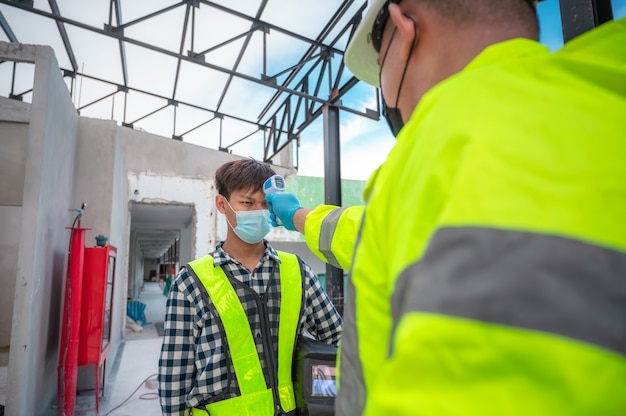 O conceito do coronavírus e a indústria da construção: supervisores de engenheiros civis medem a temperatura dos trabalhadores da construção civil nos canteiros de obras. teste de febre Medir a temperatura no canteiro de obras.