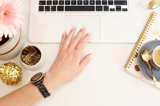 O conceito feminino no local de trabalho no plano coloca o estilo com o portátil, o café, as flores, o abacaxi dourado, o caderno e os clipes de papel, mão da mulher. Blogger trabalhando. Vista de cima, brilhante, rosa e dourado