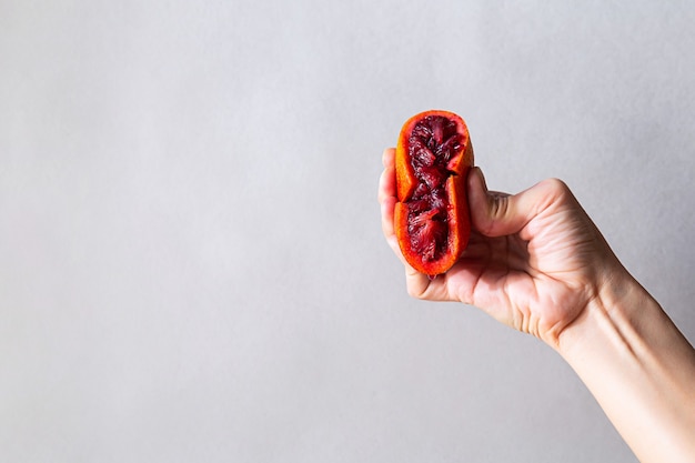 O conceito moderno de alimentação saudável, a mão feminina segura metade de uma fruta laranja vermelha