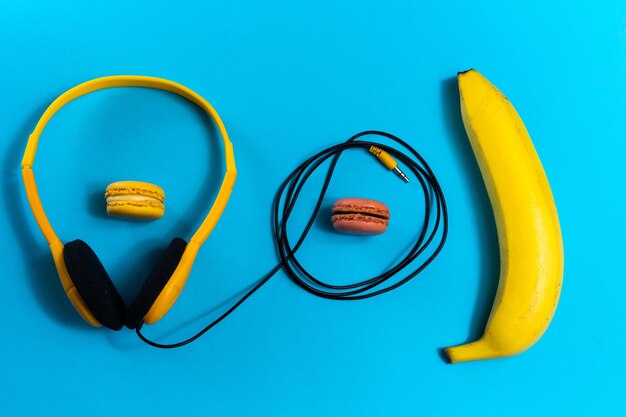 Foto o conceito plano de minimalismo ouve uma música banana de fones de ouvido sobre fundo azul vista superior