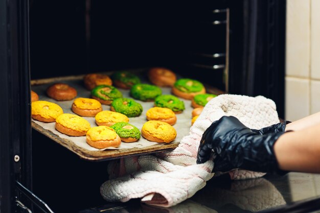 O confeiteiro tira uma assadeira com doces redondos verdes e amarelos do forno. profiteroles crocantes de craquelure