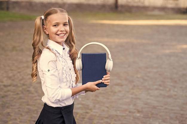 O conhecimento assimila melhor dessa maneira Conceito de livro de áudio Tecnologias digitais para aprender E-learning e métodos modernos Menina bonita estudante segura livro e fones de ouvido Ouvindo livro escolar