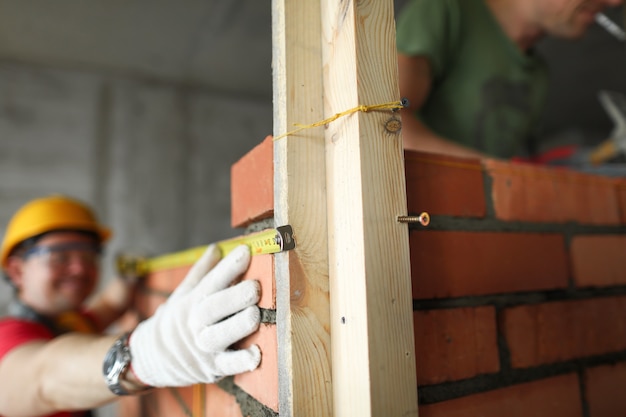 O construtor faz medições com uma fita métrica na alvenaria.