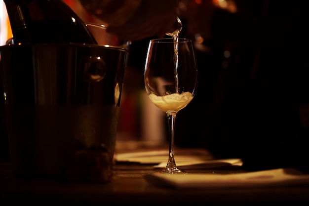 O copo de vinho iluminado está sobre a mesa e uma gota de champanhe rosa é despejada nele.