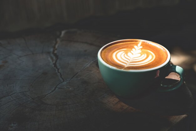 O copo do café do latte está sobre a tabela de madeira com sombra e luz do sol.