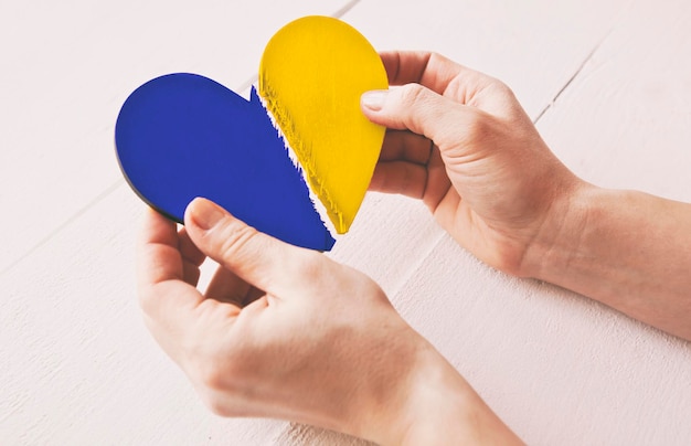 Foto o coração de madeira partido nas cores da bandeira ucraniana nas mãos da mulher