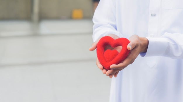 O coração do símbolo vermelho na mão do sacerdote ou a mão do homem.