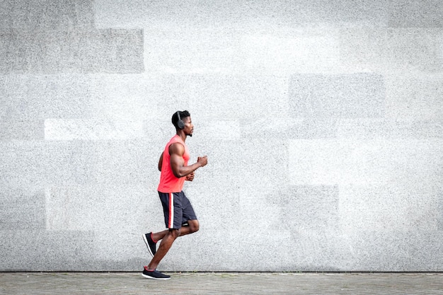 O corredor afro-americano corre rápido para a frente contra o fundo da parede da cidade