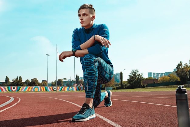 O corredor masculino em forma esticando as pernas se preparando para correr durante o treinamento nas pistas do estádio. O atleta, fitness, treino, esporte, exercício, treinamento, Atlético, conceito de estilo de vida