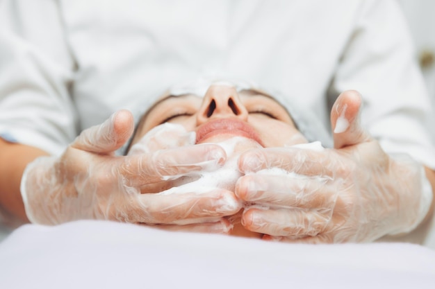 O cosmetologista limpa a pele com espuma procedimento de cuidados com a pele de uma mulher cosméticos naturais um rosto bonito tratamento cosmético do rosto creme de peeling terapêutico