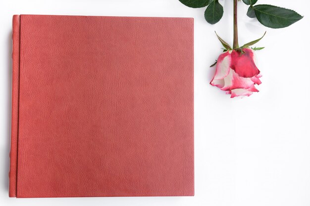 O couro vermelho cobriu o álbum do casamento e a rosa encontra-se no fundo branco.