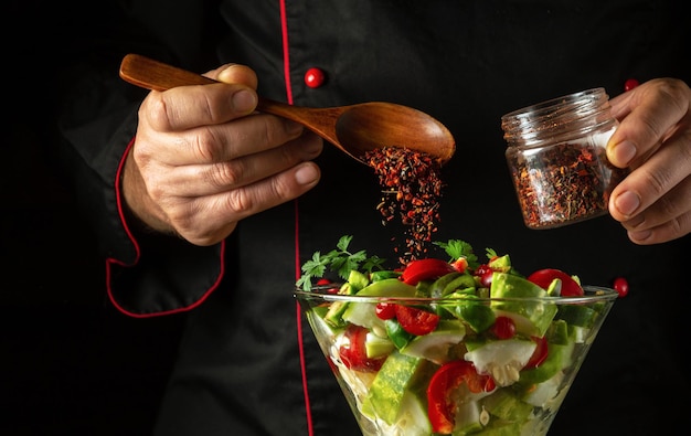 O cozinheiro adiciona especiarias aromáticas a uma salada de vitaminas para o almoço O conceito de preparar um prato vegetariano com as mãos de um cozinheiro Prato de vegetais em uma tigela
