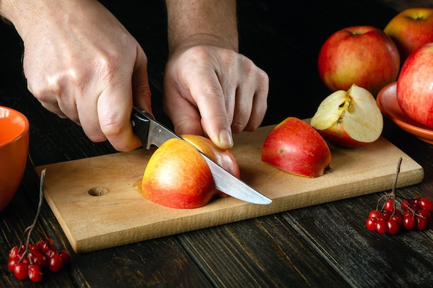 O cozinheiro corta a maçã em uma tábua para fazer compota ou suco de frutas Maçãs dieta para um conjunto de vitaminas Ambiente de trabalho na mesa da cozinha