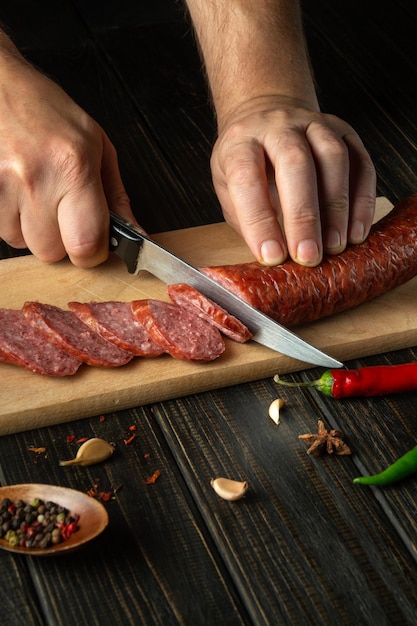 O cozinheiro corta a salsicha em pedaços pequenos para fazer sanduíches Idéia de comida de rua