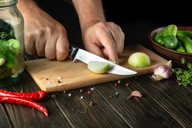 O cozinheiro corta cebolas frescas para decapagem com especiarias e pepinos Closeup das mãos do chef enquanto trabalhava na mesa da cozinha Lugar para publicidade