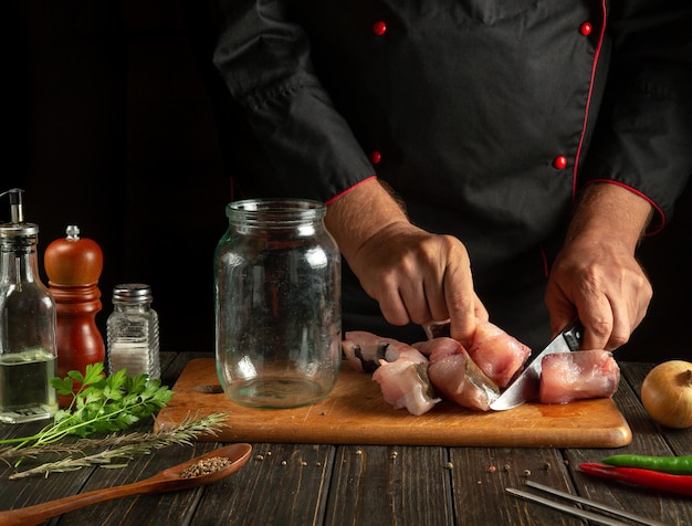 O cozinheiro corta o peixe carpa para preparar o arenque em um frasco com especiarias O conceito de salgar o peixe em casa