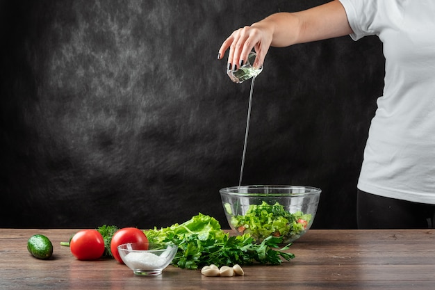 O cozinheiro da mulher adiciona o azeite à salada, cozinhando a salada na madeira.