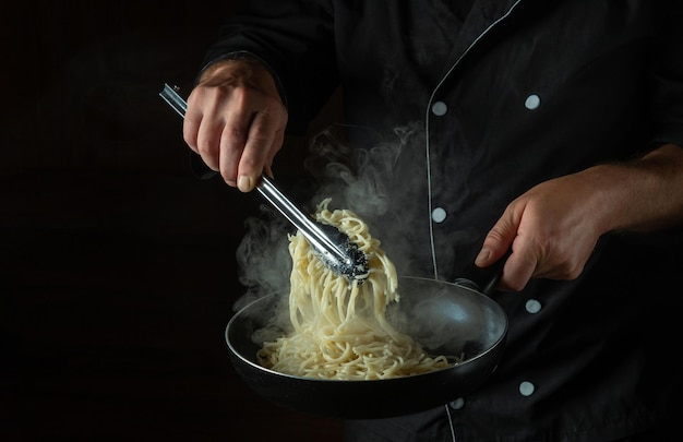 O cozinheiro frita espaguete em uma panela quente Espaço para publicidade em um fundo preto