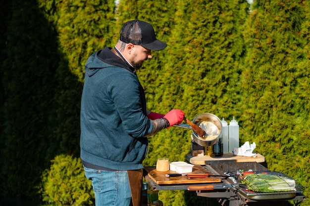 O cozinheiro mistura comida em uma panela conceito do cozimento correto da carne o chef prepara batatas fritas um bife ao ar livre chef derrama molho na carne