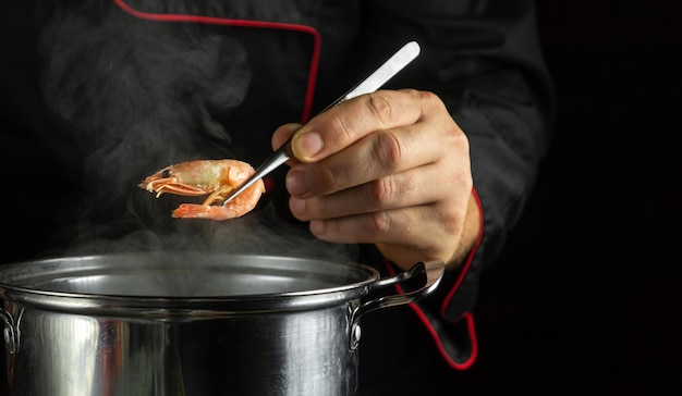 O cozinheiro na panela prepara os camarões O cozinheiro verifica a prontidão dos camarões